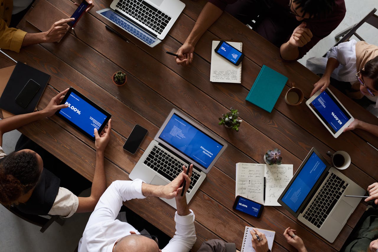 home-img Overhead view of a diverse team discussing around a wooden table, using technology.